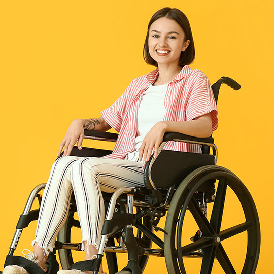 acp-law-1-02 Person in a striped shirt and white pants sitting in a wheelchair against a yellow background.