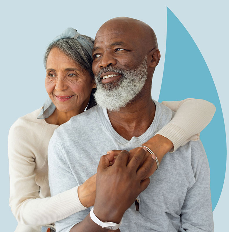 Two people hugging, one wearing a grey sweater and the other in beige, against a blue backdrop.