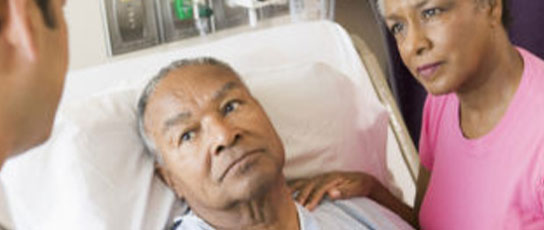 Narrow-Block-6 Two individuals in conversation beside a hospital bed.