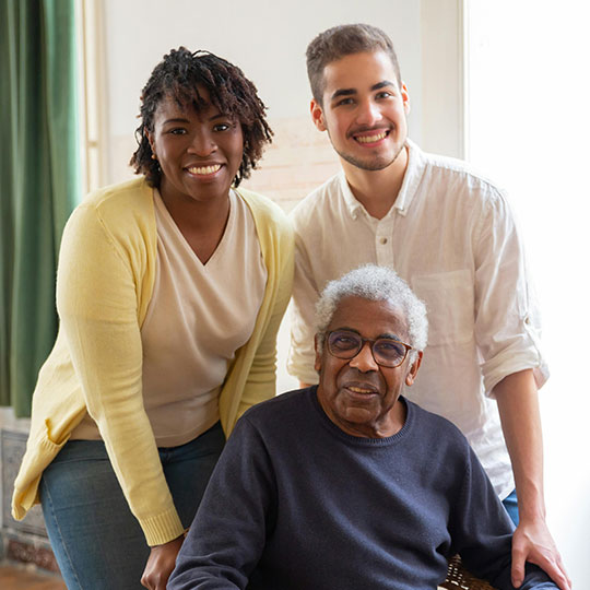 People-Block-12 Three people in casual attire posing indoors, two standing and one seated.