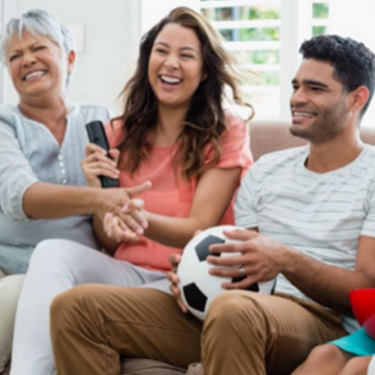People-Block-30 Three people on a sofa with one holding a soccer ball and another with a remote control.