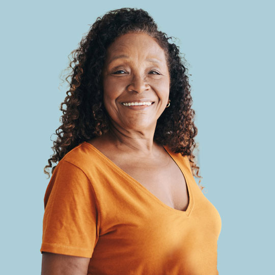 People-Block-35 Person in an orange shirt with curly hair, standing against a blue background.